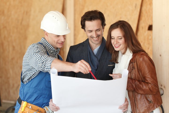 Worker shows house design plans to a young couple at construction site