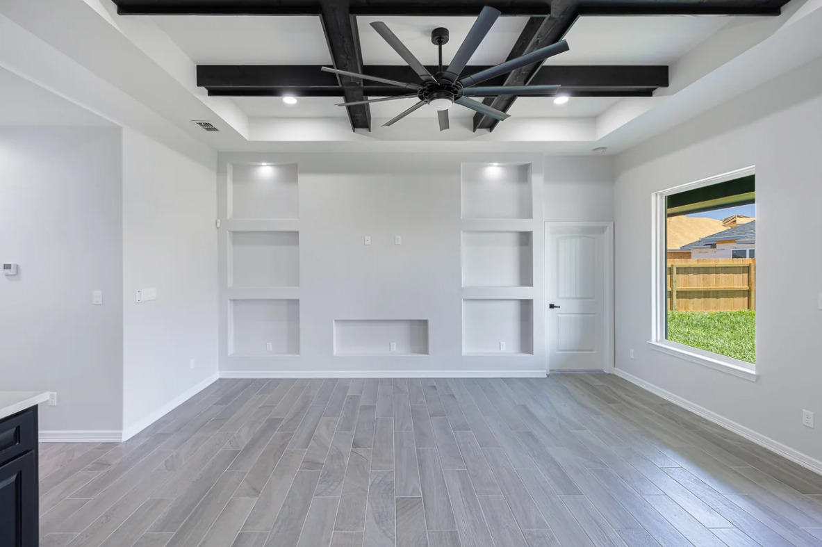 Entertainment Wall by Villanueva Construction. Modern white living room with a ceiling fan and wood flooring, highlighting stylish entertainment wall ideas for Texas homes.