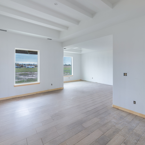 Spacious unfinished interior with large windows and wooden flooring, ready for design.